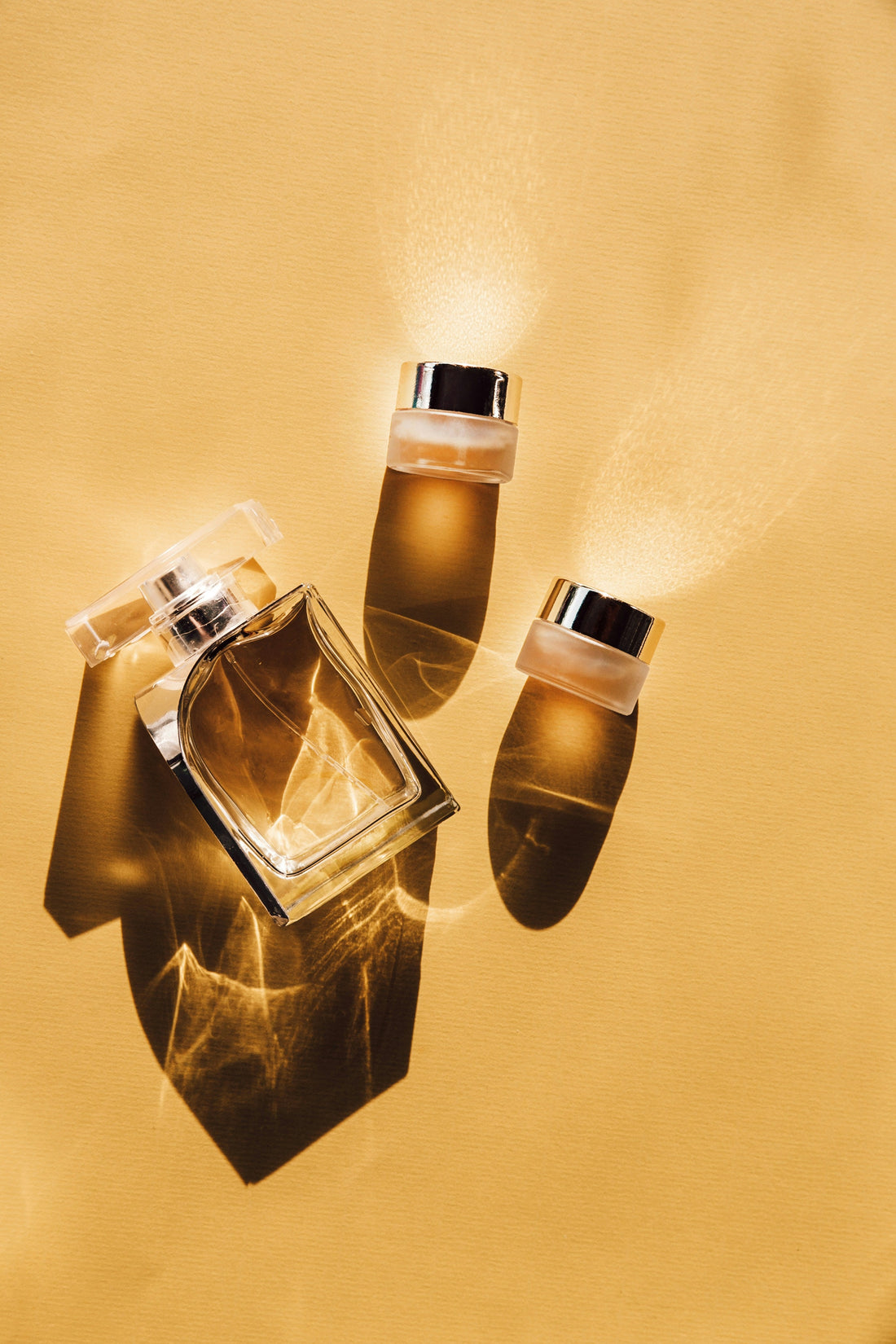 Top down view of luxury fragrance on yellow flat background, with one spray bottle and two smaller refill bottles, niche fragrance